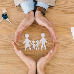 Couple making circle with hands on wooden table with paper people inside, family insurance